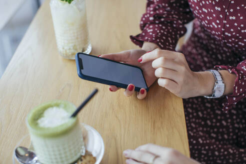 Frau hält Smartphone in einem Cafe - MOMF00773