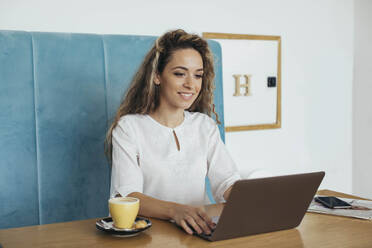 Woman having coffee in a cafe and looking at laptop - MOMF00785