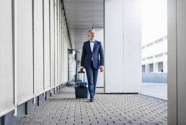 Mature businessman in a passageway with rolling suitcase on the go - DIGF08513