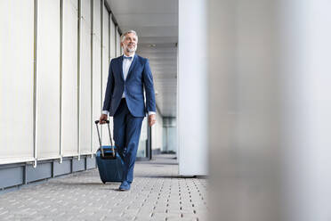 Mature businessman in a passageway with rolling suitcase on the go - DIGF08514