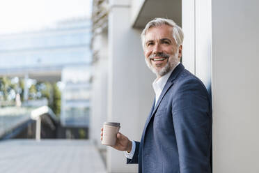 Portrait of smiling mature businessman with takeaway coffee in the city - DIGF08527