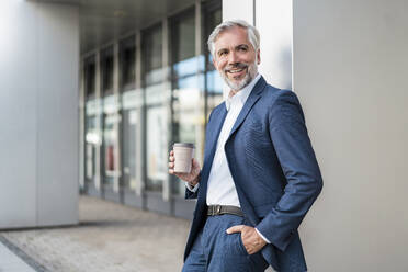 Lächelnder reifer Geschäftsmann mit Kaffee zum Mitnehmen in der Stadt - DIGF08528