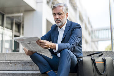 Älterer Geschäftsmann sitzt auf einer Treppe in der Stadt und liest Zeitung - DIGF08530