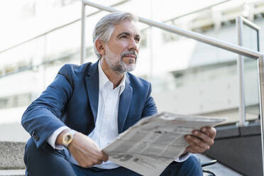 Älterer Geschäftsmann sitzt mit Zeitung auf einer Treppe in der Stadt - DIGF08534