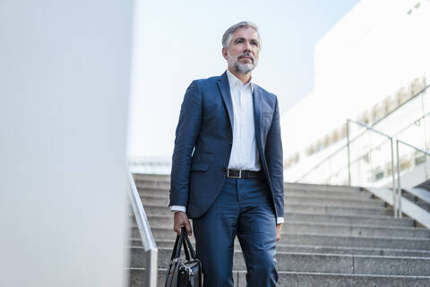 Älterer Geschäftsmann mit Tasche, der in der Stadt eine Treppe hinuntergeht, lizenzfreies Stockfoto