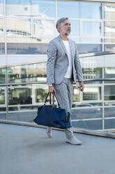 Fashionable mature businessman with travelling bag on the go - DIGF08555