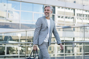 Smiling fashionable mature businessman with bag on the go - DIGF08557