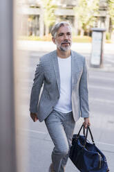 Fashionable mature businessman with travelling bag on the go in the city - DIGF08568