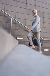 Fashionable mature businessman with bag walking up stairs - DIGF08570