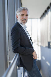 Portrait of mature businessman leaning on railing in a passageway - DIGF08594