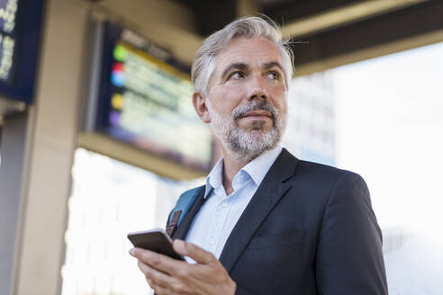 Porträt eines reifen Geschäftsmannes mit Mobiltelefon auf dem Bahnhof - DIGF08596