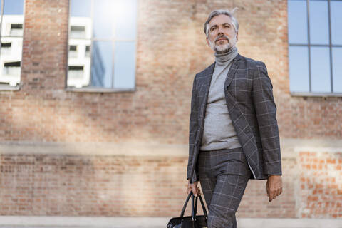 Modischer reifer Geschäftsmann mit Tasche unterwegs in der Stadt, lizenzfreies Stockfoto