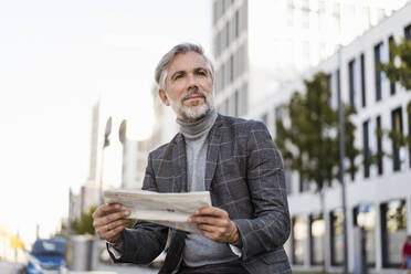 Fashionable mature businessman reading newspaper in the city - DIGF08618