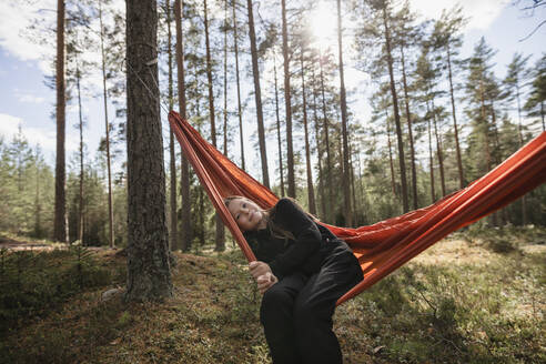 Junge Frau sitzt in Hängematte im Wald - JOHF04415