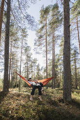 Young couple lying in hammock in forest - JOHF04416