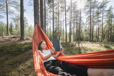 Teenager-Mädchen liest Buch in Hängematte im Wald - JOHF04419