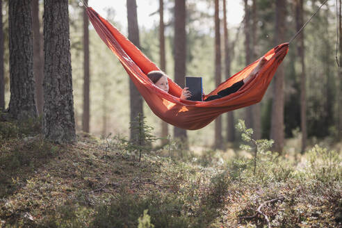 Teenager-Mädchen liest Buch in Hängematte im Wald - JOHF04421