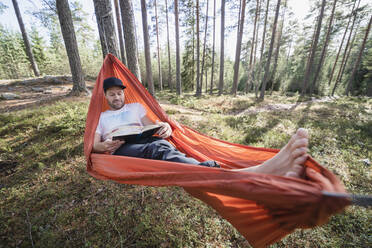 Mann liest Buch in Hängematte im Wald - JOHF04423