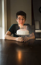 Ein Teenager bläst die Kerzen auf seinem Geburtstagskuchen am Tisch aus. - CAVF65892
