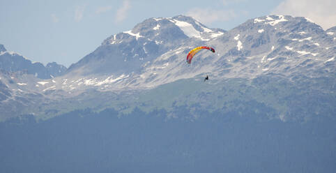 Paragliders fly high above snow covered mountains on a sunny day. - CAVF65918