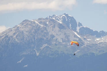 Gleitschirmflieger fliegen an einem sonnigen Tag hoch über schneebedeckte Berge. - CAVF65919
