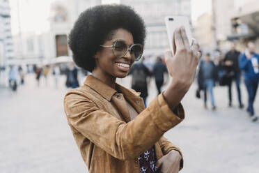 Young woman with afro hair taking selfie in city - CUF52560