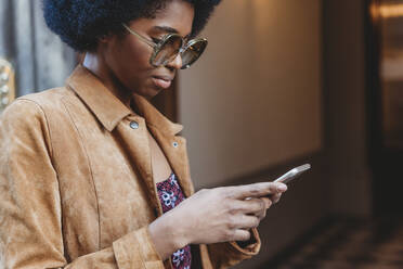 Junge Frau mit Afro-Haar, die vor einem Gebäude ihr Smartphone benutzt - CUF52561