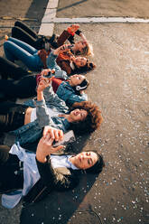 Freunde, die zusammen auf dem Bordstein ein Selfie machen und Smartphones benutzen, Mailand, Italien - CUF52584