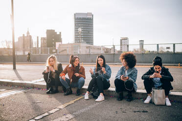 Freunde sitzen auf dem Bordstein und benutzen ihr Smartphone, Mailand, Italien - CUF52618