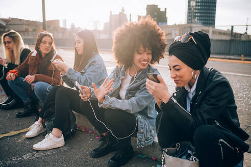 Freunde sitzen auf dem Bordstein und benutzen ihr Smartphone, Mailand, Italien - CUF52619