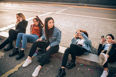 Friends together on kerb, Milan, Italy - CUF52621