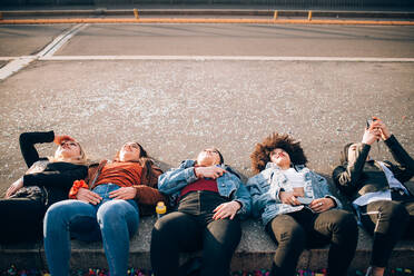 Friends lying on kerb, Milan, Italy - CUF52623