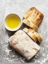 Stilleben eines bemehlten und eines unbemehlten Ciabatta-Brotes auf einem Backblech mit einer Schale Olivenöl, Draufsicht - CUF52643