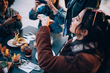 Friends taking photos of their food and drinks at outdoor cafe, Milan, Italy - CUF52708