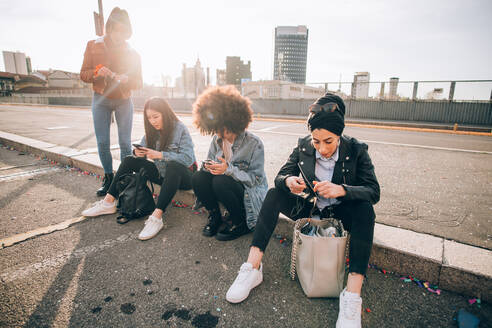 Freunde sitzen auf dem Bordstein und schreiben SMS, Mailand, Italien - CUF52733