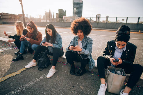 Freunde sitzen auf dem Bordstein und schreiben SMS, Mailand, Italien - CUF52734