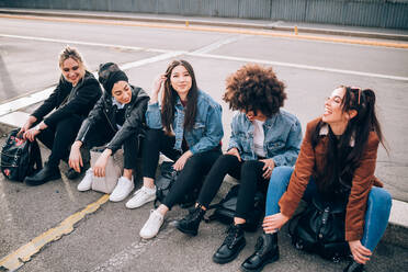 Friends sitting on kerb, Milan, Italy - CUF52761