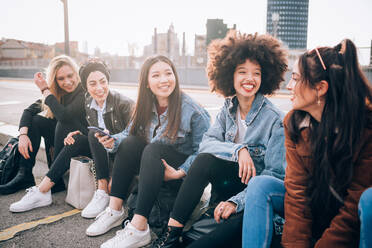 Friends sitting on kerb, Milan, Italy - CUF52763