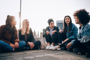 Friends sitting on kerb, Milan, Italy - CUF52766