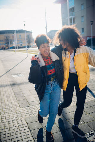 Zwei coole junge Freundinnen lachen auf einem städtischen Bürgersteig, lizenzfreies Stockfoto