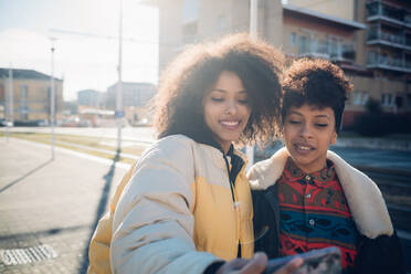 Zwei coole junge Freundinnen machen ein Smartphone-Selfie auf einem städtischen Bürgersteig - CUF52791