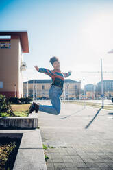 Young woman jumping from wall on urban sidewalk, full length portrait - CUF52793