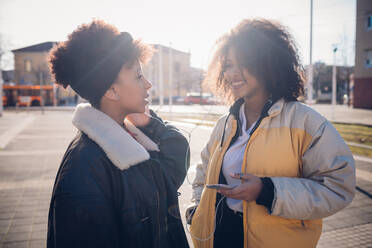 Zwei coole junge Freundinnen teilen sich Kopfhörer auf dem Bürgersteig - CUF52799