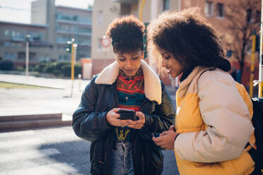 Zwei coole junge Frauen schauen auf dem Bürgersteig auf ihr Smartphone - CUF52805