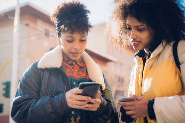 Zwei coole junge Frauen schauen auf dem Bürgersteig auf ihr Smartphone - CUF52806
