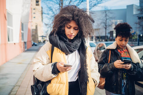 Zwei coole junge Frauen spazieren und schauen auf dem Bürgersteig in der Stadt auf ihr Smartphone - CUF52811