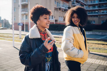 Zwei junge Frauen gehen und unterhalten sich auf einem städtischen Bürgersteig - CUF52814