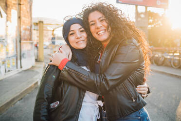 Junge Frau im Hidschab und beste Freundin umarmen sich in der Stadt, Porträt - CUF52841