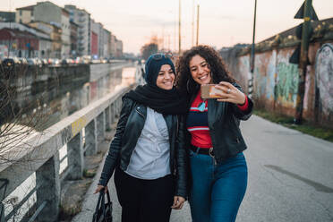 Junge Frau im Hidschab und beste Freundin machen Selfie am Stadtkanal - CUF52847