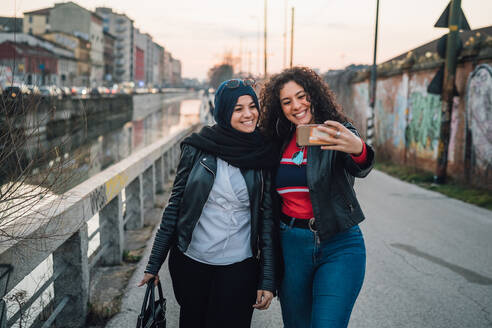 Junge Frau im Hidschab und beste Freundin machen Selfie am Stadtkanal - CUF52847